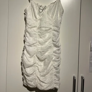 Vit klänning - Säljer en elegant vit klänning med ett vackert draperat mönster. Klänningen har en åtsittande passform och är perfekt för festliga tillfällen.