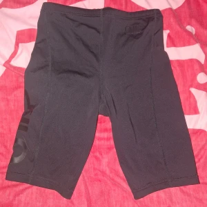 Svarta kompressionsshorts från OTP - Säljer ett par svarta kompressionsshorts från OTP. De har en tight passform och är perfekta för träning. Shortsen har en diskret logga på sidan och snörning i midjan för justerbar passform.