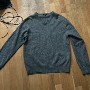 Grå v-ringad tröja från GANT - Säljer en stilren grå v-ringad tröja från GANT. Tröjan är långärmad och har ribbade muddar vid ärmslut och nederkant. Ett litet hål i höger armbåge. Nypris cirka 1000