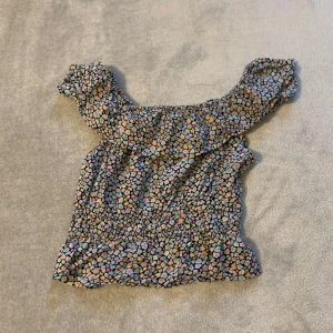 Mönstrad offshoulder topp - Säljer en färgglad offshoulder topp med ett unikt mönster i olika pastellfärger. Toppen har en smickrande passform med volangdetaljer vid axlarna och midjan. Perfekt för en somrig look!