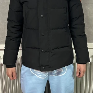 Svart dunjacka från Canada Goose - Säljer en svart dunjacka från Canada Goose med huva och knäppning framtill. Jackan har långa ärmar och en klassisk pufferdesign. Den sitter bra på S men är XS. 