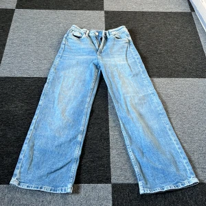 Blå wide leg jeans från H&M - Säljer ett par blå wide leg jeans från H&M med justerbar midja och hög midja. De har en dragkedja och knapp framtill. Perfekta för en avslappnad stil.
