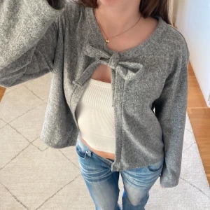 Grå kofta med rosett - Säljer en mysig grå kofta med knyte framtill. Storlek L men sitter mer so men S🥰skriv vid funderingar!!💕💕