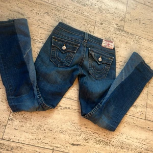 Blå jeans från True Religion - Snygga blå jeans från True religion. De var från början skinny men insydda till boot cut. De har en klassisk femficksdesign och en knappdetalj på bakfickorna. Säljer för att de är för stora. 
