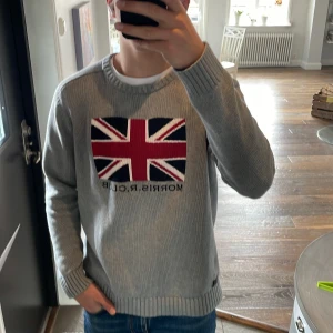 Grå tröja från Morris R. Club - Säljer en grå stickad tröja från Morris med union Jack flaggan på bröstet. Tröjan är i bra skick är är perfekt till ett par jeans. Modellen är 183 och väger 74 kg