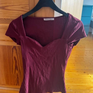 Vinröd ribbad topp från Anna Field - Snygg vinröd topp från Anna Field med ribbad struktur och korta ärmar. Den har en v-ringad design som ger en elegant touch. Perfekt för att lyfta vilken outfit som helst!