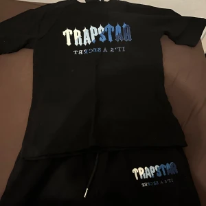 Svart t-shirt från Trapstar - Snygg svart t-shirt från Trapstar med ett coolt tryck i blått och vitt på framsidan. Perfekt för en avslappnad stil. Perfekt till sommaren