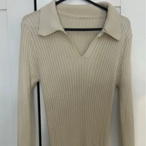 Beige ribbad långklänning - Snygg beige ribbad långklänning med v-ringning och krage. Perfekt för en stilren look. Långärmad design.