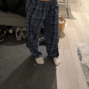 Blå rutiga byxor - Säljer ett par bekväma blå rutiga byxor med elastisk midja. Byxorna har en loose passform och är perfekta för en avslappnad stil. De har ett klassiskt rutmönster i olika nyanser av blått.