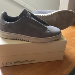  Axel Arigato laceless - Snygga grå sneakers från Axel Arigato i mocka. Skorna har en stilren design med rund tå och en vit sula. Perfekta för en avslappnad och trendig look. Endast använd 4 ggr. Dustbag och kartong medföljer 