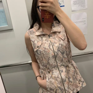 Mönstrad väst Weekends - Snygg väst med ormmönster från Weekends. Västen har dragkedja framtill och praktiska fickor med knappar. Den är ärmlös och har en justerbar midja för en perfekt passform.