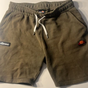Olivgröna shorts från Ellesse - Säljer ett par olivgröna shorts från Ellesse med elastisk midja och vit snörning. Shortsen har två sidofickor och Ellesse-logga på framsidan. Perfekta för en avslappnad stil.