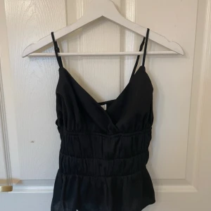 Svart linnetopp från Pekyol - Snygg svart linnetopp från Pekyol med justerbara axelband och v-ringning. Toppen har en smickrande passform med rynkade detaljer och en lätt volang nedtill. Perfekt för en stilren look. Väldigt liten i storlek själv kan jag bära den och har S
