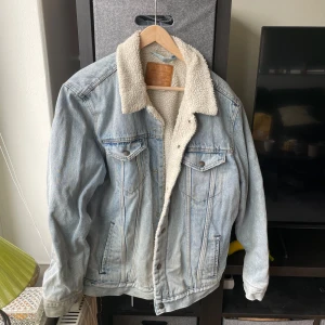 Ljusblå jeansjacka med teddyfoder från Levi's - Säljer en snygg ljusblå jeansjacka från Levi's med mysigt teddyfoder. Jackan har en klassisk design med två bröstfickor och knappar framtill. Perfekt för kyligare dagar när du vill hålla stilen. 🧥✨