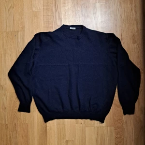 Mörkblå tröja från Gran Sasso - Snygg mörkblå tröja från Gran Sasso, tillverkad i ull. Tröjan har en klassisk design med rund hals och långa ärmar. Perfekt för en stilren look. Sitter som en liten M. Ett par lagningar som knappt märks av.