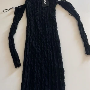 Svart ribbad klänning - Snygg svart ribbad klänning med långärmad design. Perfekt för en stilren look. Klänningen har en åtsittande passform och är tillverkad i ett stretchigt material för extra komfort.