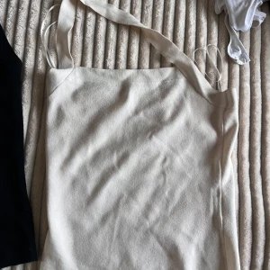 Beige och svart ribbad linnetopp från H&M - Säljer två ribbade linnetoppar från H&M i storlek S. En i beige och en i svart. Perfekta för sommaren med sin enkla och stilrena design. Topparna har breda axelband och en rak halslinje. Den svarta är i storlek s och den vita i m. För båda 120:-