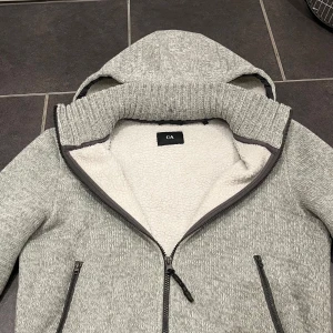 Grå fleecefodrad jacka med huva - Säljer en grå jacka från C&A med fleecefoder och huva. Jackan har dragkedja framtill och två fickor med dragkedjor. Perfekt för kyliga dagar med sin mjuka och varma insida.