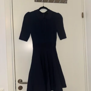 Mörkblå klänning med krage Ted baker - Elegant mörkblå klänning med krage och korta ärmar. Perfekt för en stilren look. Klänningen har en figursydd passform upptill och en lätt utsvängd kjol.