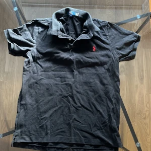 Ralph Lauren piké - Säljer en klassisk svart pikétröja från Ralph Lauren i storlek M. Tröjan har korta ärmar och en stilren krage med knappar. Perfekt för en avslappnad men ändå stilren look. 