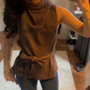 Brun ärmlös topp med knytband - Snygg brun ärmlös topp med knytband i midjan. Perfekt för en stilren look. Tillverkad i ett mjukt material som ger en bekväm passform.