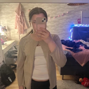 Beige glittrig kofta - Säljer en snygg beige kofta med glittrande effekt. Den har långa ärmar och knappar framtill. Perfekt för att lägga till lite glamour i vardagen. Passar bra till både jeans och kjol.