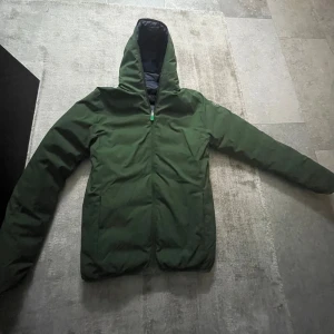 Grön och marinblå jacka från Save the Duck - Säljer en vändbar jacka från Save the Duck i grön och marinblå färg. Jackan har en dragkedja och är långärmad. Perfekt för kyligare dagar med sin quiltade design på den marinblå sidan.