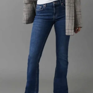 Blå bootcut jeans - Snygga blå bootcut jeans med klassisk femficksdesign och knappgylf. Perfekta för en avslappnad stil med en touch av retro. Passar bra med både sneakers och klackar.