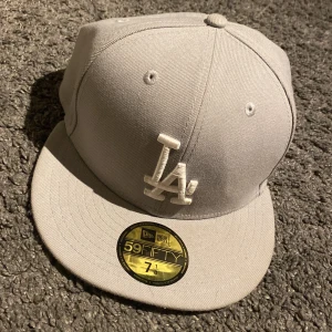 Grå keps från New Era - Snygg grå keps från New Era med broderad LA-logga framtill. har en klassisk passform. Perfekt för att ge din outfit en sportig touch. Säljer för de inte min stil inte använd mycket den är fresh postas i kartong så skärmen ej böjs det är storlek 56,8 cm nypris 500 mitt 150kr 