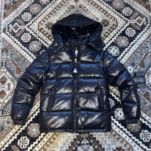 Svart pufferjacka från Moncler - Säljer en snygg svart pufferjacka från Moncler med avtagbar huva. Jackan har en glansig finish och dragkedja framtill. Perfekt för kyliga dagar med sin vadderade design.STORLEK S