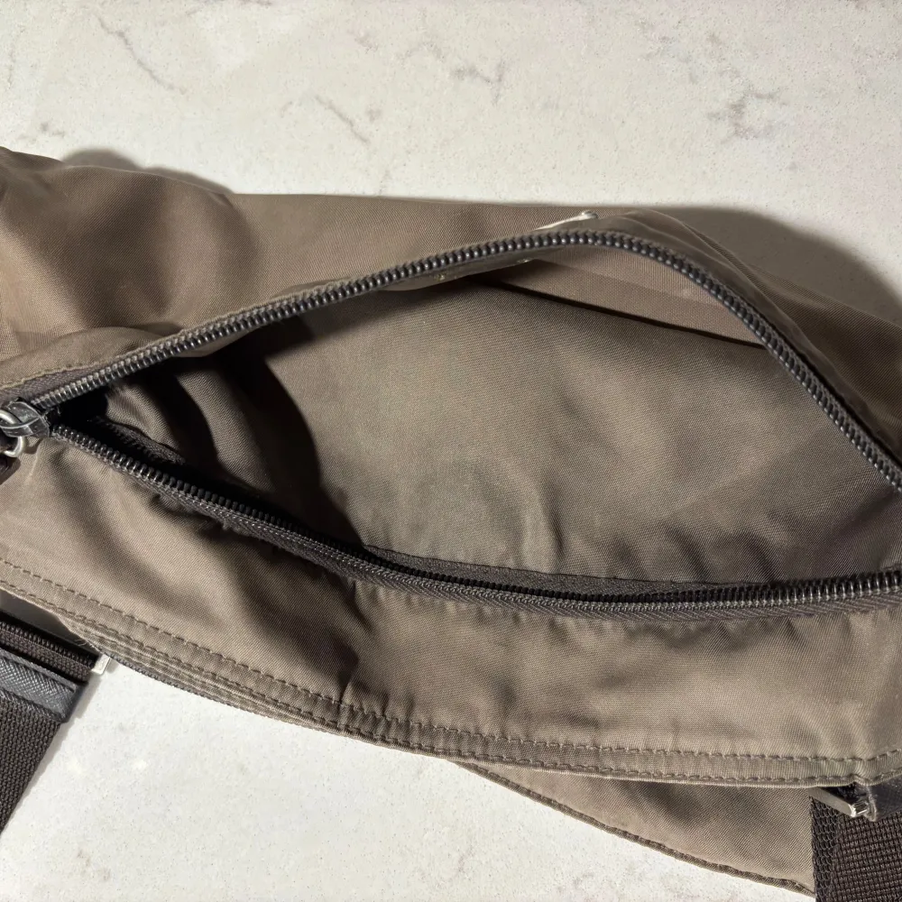 Snygg grön/bron axelväska från Prada med justerbar axelrem. Väskan har en stilren design med en diskret logotyp på framsidan. Perfekt för att bära dina dagliga nödvändigheter med stil. (I använda skick, 7/10). Laukut & Käsilaukut.