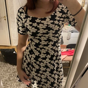 Känning - Säljer en söt svart klänning med vita blommor. Den har korta ärmar och en smickrande passform. Perfekt för en dag ute eller en avslappnad kväll. 🌼