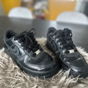 Svarta Nike sneakers - Snygga svarta Nike sneakers med klassisk design och snörning. Perfekta för en stilren look. Skorna har en metallisk detalj på snörena och är tillverkade i skinn.