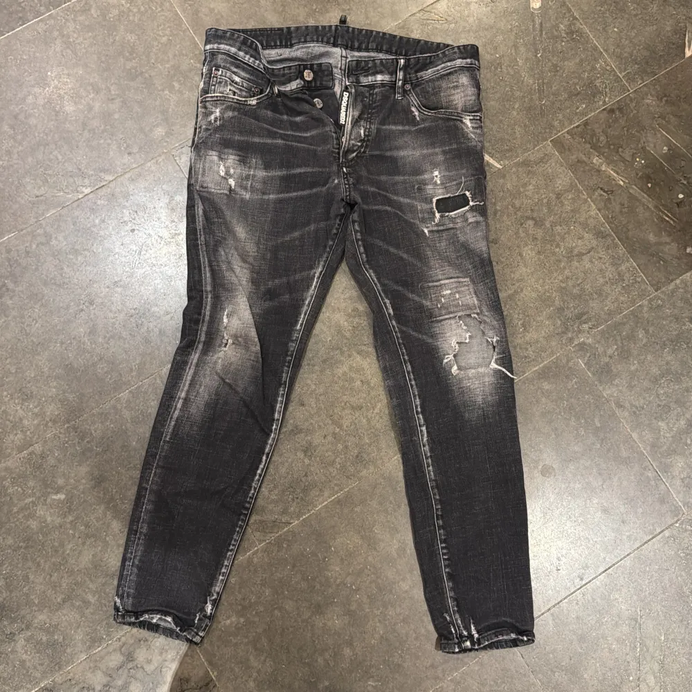 Snygga svarta jeans från Dsquared2 med slitna detaljer och en cool, tvättad look. De har knappar i gylfen och en klassisk femficksdesign. Perfekta för en trendig och avslappnad stil.. Farkut & Housut.