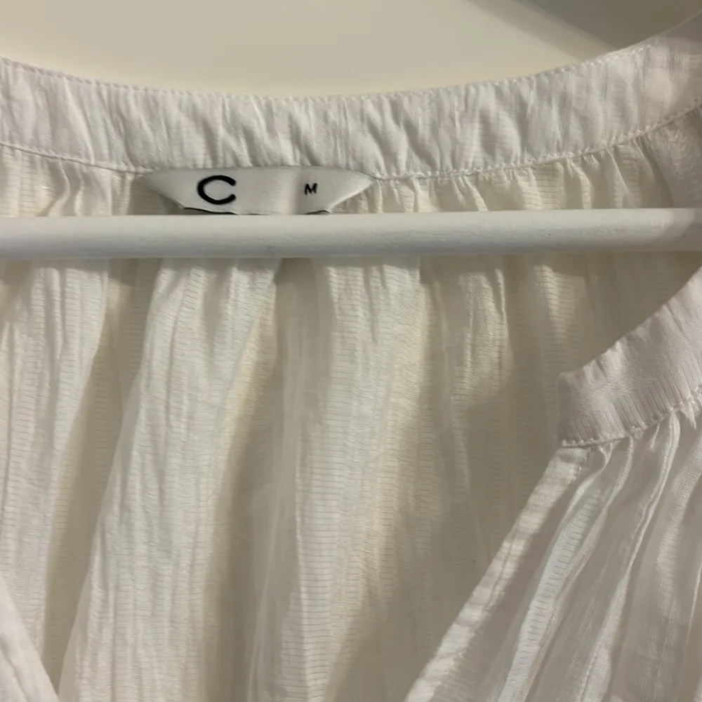 Säljer en luftig vit blus från märket C. Blusen har korta ärmar och en v-ringad design som ger en avslappnad look. Perfekt för varmare dagar eller som en stilren bas i garderoben.. Yläosat.