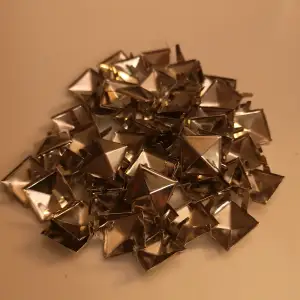 Säljer en samling av silvriga pyramidformade nitar. 53 st nitar lätta att sätta fast med piggarna på baksidan. 1cm 