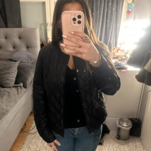 Svart quiltad jacka - Säljer en stilren svart quiltad jacka med knappar. Perfekt för kyligare dagar och ger en snygg look. Jackan har långa ärmar och en normal passform. Passar bra till både jeans och kjol.