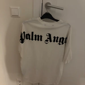 Vit t-shirt från Palm Angels - Säljer en vit t-shirt från Palm Angels med stort svart tryck på baksidan. T-shirten har en klassisk rund hals och korta ärmar. Perfekt för en stilren och avslappnad look.
