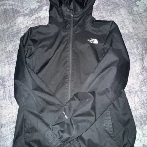 Svart vindjacka från The North Face - Säljer en svart vindjacka från The North Face med huva och dragkedja. Perfekt för blåsiga dagar och har en stilren design med logotyp på bröstet. Jackan är lätt och smidig att bära med sig. 8/10 skick, passar storlek xs,S