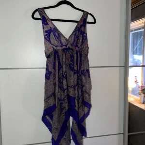 Mönstrad klänning från VJ Style - Säljer en snygg mönstrad klänning från VJ Style i lila och blå toner. Klänningen har en omlott-design med breda axelband och en luftig passform. Perfekt för varma dagar med sitt lätta material och vackra mönster.