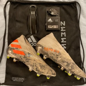 Adidas Nemeziz fotbollsskor - Säljer ett par Adidas Nemeziz 360 Agility fotbollsskor med en unik design i grått och orange med ”beetlejuice🇸🇪” skrivet på sidorna. Inkluderar originalpåse, skohorn och skruvdobbar med skruvmejsel. Storlek 42.