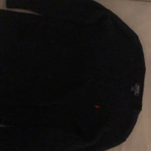 Mörkblå stickad tröja från Ralph Lauren - Säljer en snygg mörkblå stickad tröja från Ralph Lauren. Tröjan har en klassisk design med långärmade ärmar och en liten röd logga på bröstet. Perfekt för kyligare dagar.