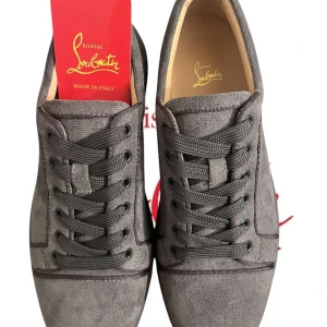 Grå sneakers från Christian Louboutin - Snygga grå sneakers i mocka från Christian Louboutin med den ikoniska röda sulan. Skorna har snörning och en stilren design som passar perfekt för en trendig look.