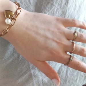Guldarmband med hjärta och pärla - Säljer smyckerna som ett set. Guldarmband med ett hjärta och vit pärla. 3 ringar. Den på lillfingret är mycket mindre än dom andra 2. Om du inte vill köpa alla för 110 skriv till mig så ordnar vi det! 🩷