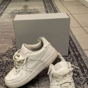 Vita Nike Air Force sneakers - Säljer ett par klassiska vita Nike Air Force sneakers. De har en stilren design med snörning och den ikoniska Nike-loggan på sidan. Perfekta för en casual look.