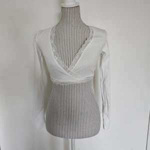 Vit omlottopp med spetsdetaljer - Sparsamt använd. Fint skick. Storlek S men uppskattar att den passar XS-S.