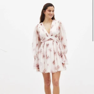 Blommig kortklänning från NA-KD - Superfin kortklänning från NA-KD i ljusa toner med blommigt mönster. Klänningen har v-ringning, markerad midja och långa, transparenta ärmar med volang vid ärmslut. Perfekt för dig som gillar romantisk och flowy stil.