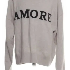 Grå tröja med svart AMORE-tryck - Snygg grå tröja med stort svart AMORE-tryck över bröstet. Tröjan har en avslappnad passform och långa ärmar, perfekt för en chill och trendig look. Enkel att matcha med jeans eller kjol för en cool vardagsstil.