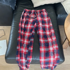 Rödblå rutiga mjukisbyxor med snörning - Snygga och sköna mjukisbyxor i rödblått rutigt mönster. Byxorna har resår och snörning i midjan för extra komfort. Perfekta för chill dagar hemma eller när du vill vara extra bekväm. Tunn och mjuk bomullskänsla.