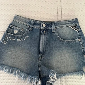 jeansshorts - Snygga blå jeansshorts från Replay med fransig kant och broderad text 'REPLAY TRUE LOVE' samt ett hjärta på fickan. Byxorna är i storlek 25💕skriv för frågor! 